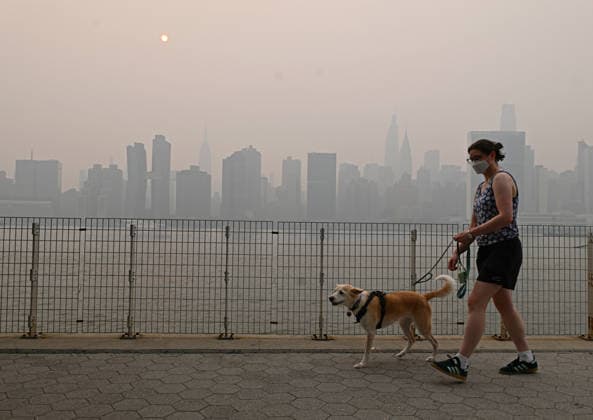July 16, 2026, New York, New York, USA: July 16, 2026 - New York, NY, USA - Masked woman walking her dog with New York City midtown skyline and the Empire State Building seen across the East River which is covered by smoke coming from the ongoing Canadian wildfires New Yorkers out with their families, friends, and pets go about their lives as they navigate the smoked filled air. (Andrea RENAULT Zuma Press) New York USA - ZUMAg115 20260716_faf_g115_050 Copyright: xAndreaxRenaultx