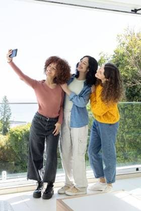 Diverse female friends posing for selfie on glass balcony overlooking water, holding smartphone, model released, property released, 02.09.2025 06:00:00, 8091131 Copyright: xIDS-260315_3xcreatorid:x0x 8091131