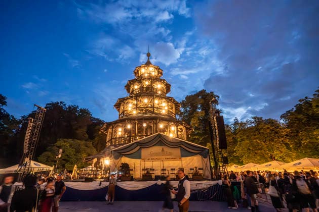 Kocherlball am Chinesischen Turm, Biertrinken bei Kerzenschein, erstes Morgengrauen um 4:30 Uhr, München, 19. Juli 2026 Deutschland, München, 19. Juli 2026, Biertrinken bei Kerzenschein, traditioneller Kocherlball am Chinesischen Turm, Englischer Garten, hier: erstes Morgengrauen um 4:30 Uhr, die Bühne für das Tanzvergnügen ab 6 Uhr steht schon bereit, manche Besucher sind schon um 3 Uhr früh im Biergarten, um noch einen Platz zu ergattern, die Menschen trinken ein Bier, essen eine Brotzeit, tragen Tracht, Tradition entstand im 19. Jahrhundert, als Hauspersonal, Dienstboten und KöchInnen in den frühen Morgenstunden vor Dienstbeginn gefeiert und getanzt haben, Tradition wurde ab 1989 wiederbelebt, traditionell am 3. Sonntag im Juli,