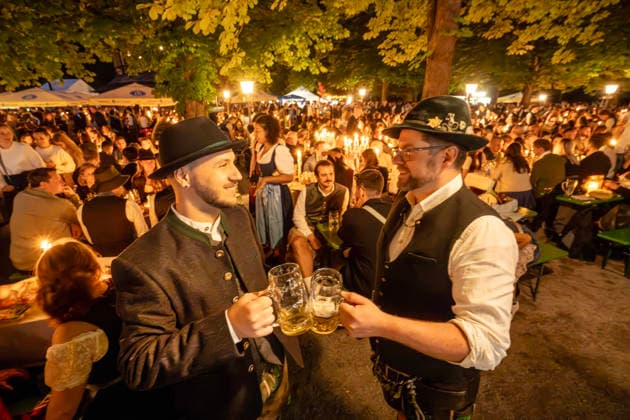 Kocherlball am Chinesischen Turm, Biertrinken bei Kerzenschein um 4:35 Uhr, München, 19. Juli 2026 Deutschland, München, 19. Juli 2026, Biertrinken bei Kerzenschein, traditioneller Kocherlball am Chinesischen Turm, Englischer Garten, zwei bayerische Besucher prosten sich um 4:35 Uhr mit ihrer halben Hellen zu, manche Besucher sind schon um 3 Uhr früh im Biergarten, um noch einen Platz zu ergattern, die Menschen trinken ein Bier, essen eine Brotzeit, tragen Tracht, Tradition entstand im 19. Jahrhundert, als Hauspersonal, Dienstboten und KöchInnen in den frühen Morgenstunden vor Dienstbeginn gefeiert und getanzt haben, Tradition wurde ab 1989 wiederbelebt, traditionell am 3. Sonntag im Juli, feiern, Tradition, traditionell, Bayern, typi