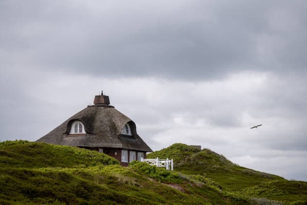 Hörnum auf Sylt 19.07.2026, Hörnum --- Ein reetgedecktes Haus liegt eingebettet in den Dünen von Hörnum auf Sylt. Die Landschaft ist von Heide und Sand geprägt. Hörnum Schleswig-Holstein Deutschland *** Hörnum on Sylt, July 19, 2026, Hörnum: A thatched-roof house nestled in the dunes of Hörnum on Sylt. The landscape is characterized by heathland and sand. Hörnum, Schleswig-Holstein, Germany