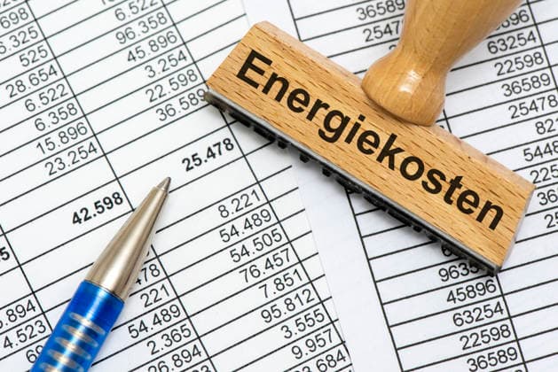 Energiekosten und Energiepreise Ein Holzstempel ist beschriftet mit dem Aufdruck Energiekosten als Symbolbild für steigende Kosten für Energie in Wirtschaft, Industrie und Handel - FOTOMONTAGE - NUR FÜR REDAKTIONELLE VERWENDUNG - *** Energy Costs and Energy Prices: A wooden stamp bears the inscription Energy Costs as a symbolic image representing rising energy costs in business, industry, and commerce. PHOTOMONTAGE FOR EDITORIAL USE ONLY