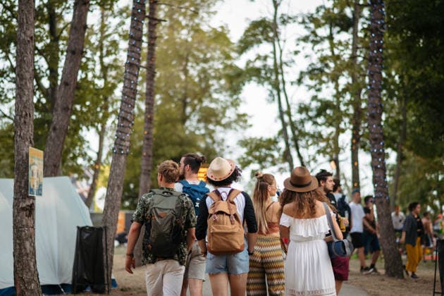 Rear view of group of young friends with backpack walking at summer festival. Rear view of group of young friends with backpack and mat walking at summer festival. model released