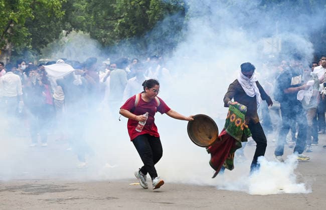 NEW DELHI, INDIA - JULY 20: CJP protestors use iron pan and wet cloth to stop tear gas hurled by Delhi Police to disperse supporters of the Cockroach Janta Party (CJP) after they gather in large numbers and breach security barricades on DR Rajendra Prasad Road near Parliament House on July 20, 2026 in New Delhi, India. The protesters were demanding the resignation of Union Education Minister Dharmendra Pradhan over alleged examination irregularities. (Photo by Ajay Aggarwal Hindustan Times) Delhi Police Use Lathi Charge And Tear Gas Shells To Disperse CJP Supporters During Their March To Parliament