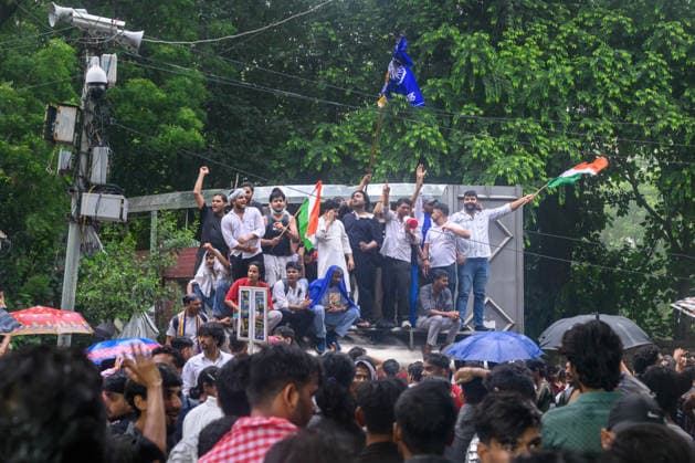 July 20, 2026, New Delhi, New Delhi, India: NEW DELHI, India Ã¢â‚¬ Protesters wave national flags and shout slogans while standing atop a barricade as others shelter under umbrellas in the rain, during demonstrations by the Cockroach Janata Party (CJP) demanding the resignation of Education Minister Dharmendra Pradhan over alleged irregularities in the NEET-UG exam, July 20, 2026. New Delhi India - ZUMAm184 20260720_zip_m184_016 Copyright: xAnkitxRoyxMajumderx