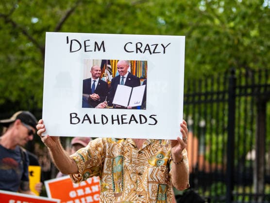 July 20, 2026, Salt Lake City, Utah, USA: A protester holds a sign reading DEM CRAZY BALDHEADS featuring a photograph of U.S. Senator Mike Lee and Utah Governor Spencer Cox outside the Utah Governor s Mansion in Salt Lake City, Utah, on Monday, July 20, 2026. The community rally was organized to protest executive actions drastically reducing the boundaries of the Bears Ears and Grand Staircase-Escalante national monuments. Salt Lake City USA  - ZUMAm292 20260720_znp_m292_078 Copyright: xCharlesxMcClintockxWilsonx