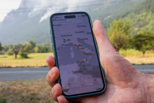 Argentiere La Bessee Wildfire - France A person holds a smartphone displaying the WaterBomber application used to track firefighting aircraft as smoke from a wildfire rises behind in L Argentiere la Bessee, the application allows residents to monitor the movements of aerial firefighting aircraft during the wildfire response, Hautes Alpes, France, July 21, 2026. Photo by Thibaut Durand ABACAPRESS.COM Argentiere La Besse Provence-Alpes-Cote d Azur France  Copyright: xDurandxThibaut ABACAx