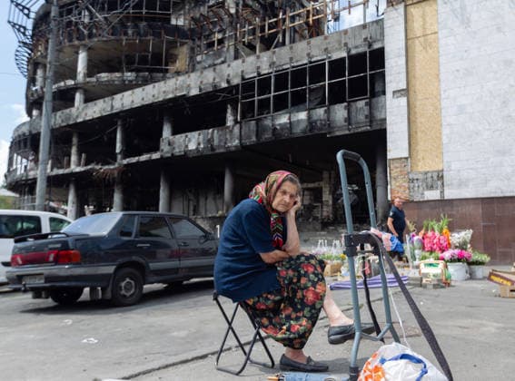 An elderly woman sitting in a folding chair sells goods in the street outside the Kvadrat shopping centre destroyed in the large-scale Russian attack on the night of May 23–24, 2026, Kyiv, Ukraine, July 21, 2026. On Sunday night, July 19, 2026, Russia launched a massive missile strike on the Ukrainian capital. The Lukianivka historical neighbourhood was hit again. The strike damaged the Lukianivska metro station, its vestibule and foyer, and wrecked the Lukianivka market. The underground passage on Yuriia Illienka Street was also directly struck. (Photo by Kyrylo Chubotin Ukrinform) Lukianivka neighbourhood in Kyiv recovers from massive Russian attack  Copyright: xKyryloxChubotinx