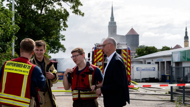 22.07.2026, Deutschland,Sachsen, Bautzen : Bautzens Oberbürgermeister Karsten Vogt (r.) spricht am Einsatzort mit Kräften der Feuerwehr. Der Brand eines Batteriespeichers am Schliebenparkplatz beschäftigt die Einsatzkräfte bereits seit vielen Stunden. Der betroffene Speichercontainer wird dauerhaft gekühlt und überwacht. *** July 22, 2026, Germany, Saxony, Bautzen: Bautzen’s mayor, Karsten Vogt, speaks with firefighters at the scene. Emergency responders have been working for many hours to extinguish a fire in a battery storage unit at the Schlieben parking lot. The affected storage container is being continuously cooled and monitored.