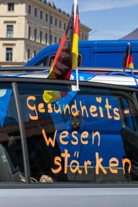 Munich, Bavaria, Germany July 25, 2026: Protesters demonstrate in downtown Munich against Chancellor Friedrich Merz (CDU) and the federal government™s policies. The rally is directed, among other things, against the government™s economic and social policies. A car with a German flag and the words Strengthen the healthcare system written on the windshield *** Teilnehmer demonstrieren in der Münchner Innenstadt gegen Bundeskanzler Friedrich Merz (CDU) und die Politik der Bundesregierung. Die Kundgebung richtet sich unter anderem gegen die Regierungs- und Sozialpolitik. Ein Auto mit Deutschlandfahne und der Aufschrift auf der Scheibe: Gesundheitswesen stärken