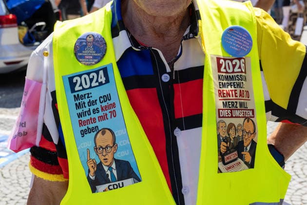 Munich, Bavaria, Germany July 25, 2026: Protesters demonstrate in downtown Munich against Chancellor Friedrich Merz (CDU) and the federal government™s policies. The rally is directed, among other things, against the government™s economic and social policies. A man is wearing a high-visibility vest featuring illustrations of Friedrich Merz and the CDU, along with slogans such as: With the CDU, there will be no retirement at 70 and Commission recommends: Retirement at 70 Merz wants to implement this *** Teilnehmer demonstrieren in der Münchner Innenstadt gegen Bundeskanzler Friedrich Merz (CDU) und die Politik der Bundesregierung. Die Kundgebung richtet sich unter anderem gegen die Regierungs- und Sozialpolitik. Ein Man