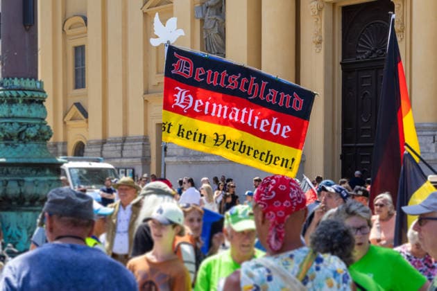 Munich, Bavaria, Germany - July 25, 2026: Protesters demonstrate in downtown Munich against Chancellor Friedrich Merz (CDU) and the federal government™s policies. The rally is directed, among other things, against the government™s policies and social policies. Banner with the inscription: Germany, love for one™s homeland is not a crime! *** Teilnehmer demonstrieren in der Münchner Innenstadt gegen Bundeskanzler Friedrich Merz (CDU) und die Politik der Bundesregierung. Die Kundgebung richtet sich unter anderem gegen die Regierungs- und Sozialpolitik.Fahne bzw. Flagge mit Aufschrift: Deutschland, Heimatliebe ist kein Verbrechen!