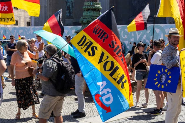 News Bilder des Tages Munich, Bavaria, Germany - July 25, 2026: Protesters demonstrate in downtown Munich against Chancellor Friedrich Merz (CDU) and the federal government™s policies. The rally is directed, among other things, against the government™s policies and social policies. A man holds a banner featuring a redesigned German flag with the inscription WIR SIND DAS VOLK? (WE ARE THE PEOPLE?) and the logo of the AfD (Alternative for Germany) party *** Teilnehmer demonstrieren in der Münchner Innenstadt gegen Bundeskanzler Friedrich Merz (CDU) und die Politik der Bundesregierung. Die Kundgebung richtet sich unter anderem gegen die Regierungs- und Sozialpolitik. Ein Mann hält eine Fahne mit einer umgestalteten Deutschlandflagge mit Aufschrift W