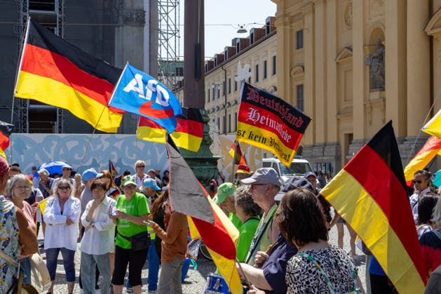 Munich, Bavaria, Germany July 25, 2026: Protesters demonstrate in downtown Munich against Chancellor Friedrich Merz (CDU) and the federal government™s policies. The rally is directed, among other things, against the government™s economic and social policies. Protesters carry German flags and a flag bearing the logo of the AfD (Alternative for Germany) party. *** Teilnehmer demonstrieren in der Münchner Innenstadt gegen Bundeskanzler Friedrich Merz (CDU) und die Politik der Bundesregierung. Die Kundgebung richtet sich unter anderem gegen die Regierungs- und Sozialpolitik. Teilnehmer mit Deutschlandfahnen und einer Fahne mit Logo der Partei AfD (Alternative für Deutschland)
