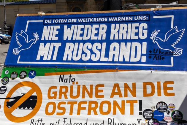 Munich, Bavaria, Germany July 25, 2026: Protesters demonstrate in downtown Munich against Chancellor Friedrich Merz (CDU) and the federal government™s policies. The rally is directed, among other things, against the government™s policies and social policies. Banners and signs read: The dead of the world wars warn us: Never again war with Russia; NATO and the Greens to the Eastern Front! Please bring bicycles and flowers *** Teilnehmer demonstrieren in der Münchner Innenstadt gegen Bundeskanzler Friedrich Merz (CDU) und die Politik der Bundesregierung. Die Kundgebung richtet sich unter anderem gegen die Regierungs- und Sozialpolitik. Banner bzw. Aufsteller mit Aufchrift: Die Toten der Weltkriege warnen uns: Nie wieder Krieg mi