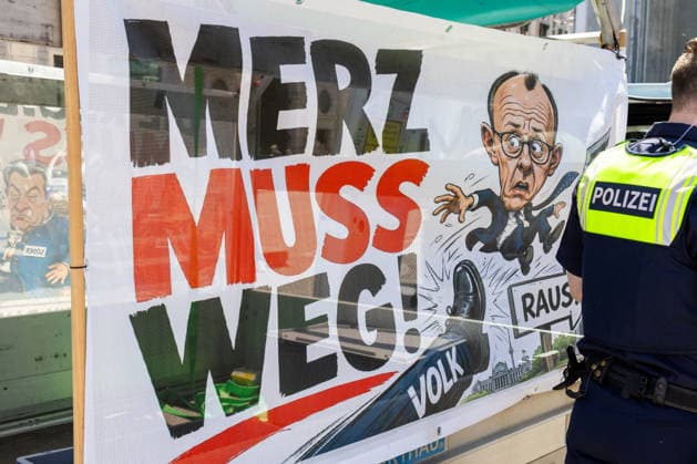 Munich, Bavaria, Germany July 25, 2026: Protesters demonstrate in downtown Munich against Chancellor Friedrich Merz (CDU) and the federal government™s policies. Among other things, the rally is directed against the government™s policies and social policies. A poster reads: MERZ MUST GO! and features an illustration of a foot kicking the chancellor with the caption: PEOPLE, and an arrow pointing through a door with the caption: GET OUT! *** Teilnehmer demonstrieren in der Münchner Innenstadt gegen Bundeskanzler Friedrich Merz (CDU) und die Politik der Bundesregierung. Die Kundgebung richtet sich unter anderem gegen die Regierungs- und Sozialpolitik. Plakat mit Aufschrift: MERZ MUSS WEG! und einer Illustration mit e