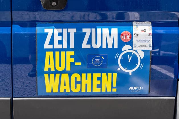 Munich, Bavaria, Germany - July 25, 2026: Protesters demonstrate in downtown Munich against Chancellor Friedrich Merz (CDU) and the federal government s policies. The rally is directed, among other things, against the government s economic and social policies. A sticker on a car reads: TIME TO WAKE UP! and features the logo of the TV station AUF1 *** Teilnehmer demonstrieren in der Münchner Innenstadt gegen Bundeskanzler Friedrich Merz (CDU) und die Politik der Bundesregierung. Die Kundgebung richtet sich unter anderem gegen die Regierungs- und Sozialpolitik. Aufkleber auf einem Auto mit Aufschrift: ZEIT ZUM AUFWACHEN! und Logo des TV-Senders AUF1