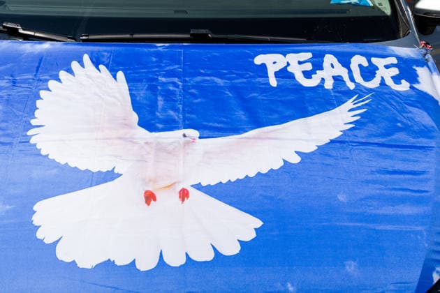 Munich, Bavaria, Germany July 25, 2026: Protesters demonstrate in downtown Munich against Chancellor Friedrich Merz (CDU) and the federal government™s policies. Among other things, the rally is directed against the government™s policies and social policies. A flag is stretched across the hood of a car, featuring a white dove of peace and the word PEACE, symbolizing peace *** Teilnehmer demonstrieren in der Münchner Innenstadt gegen Bundeskanzler Friedrich Merz (CDU) und die Politik der Bundesregierung. Die Kundgebung richtet sich unter anderem gegen die Regierungs- und Sozialpolitik. Eine Fahne bzw. Flagge ist auf der Motorhaube von einem Auto gespannt mit einer weißen Friedenstaube, Taube und dem Schriftzug PEACE, steht fü