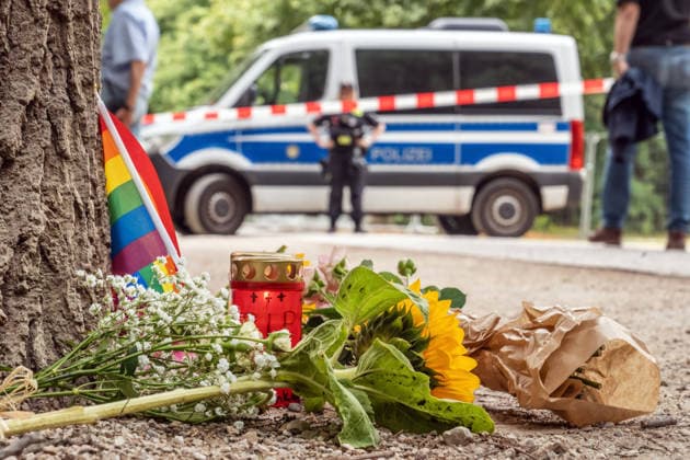 Tatort CSD-Anschlag am Ahornsteig im Tiergarten, Passanten haben zum Gedenken eine Regenbogenfahne, eine Kerze und Sonnenblumen niedergelegt, Citroen Transporter krachte hier gestern Abend vor einen Baum, Berlin, 26. Juli 2026 Deutschland, Berlin, 26. Juli 2026, Tatort CSD-Anschlag am Ahornsteig im Tiergarten, Passanten haben 80 Meter vom Tatort eine Regenbogenfahne, ein Grablicht und Sonnenblumen niedergelegt, einen Erinnerungsort geschaffen, ein Polizeifahrzeug riegelt den Bereich ab, dahinter steht noch immer der Citroen Transporter, der hier gestern Abend vor einen Baum krachte, Polizei untersucht Transporter und Anschlagsort, Szene am Sonntagmorgen um 11:45 Uhr, 14 Stunden nach dem Terroranschlag, bei dem ein Mensch starb und weitere t