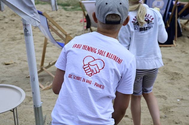 Ein Schüler trägt ein T-Shirt mit der Aufschrift: Frau Hennig soll bleiben. Sie gehört zu uns. Elternprotest - Grundschule Schöpstal droht Lehrerverlust. Große Unruhe zum Ferienbeginn an der Grundschule Schöpstal in Kunnersdorf: Einer langjährigen Klassenlehrerin droht im neuen Schuljahr die vollständige Abordnung an eine andere Schule. Da eine finale Entscheidung des Landesamtes für Schule und Bildung (LaSuB) noch aussteht, blicken viele Familien voller Ungewissheit auf die künftige Unterrichtsversorgung. Die Elternschaft wehrt sich nun massiv gegen den drohenden Unterrichtsausfall, den sie in der Vergangenheit bereits durch private Honorarkräfte im Sportunterricht abfedern musste. Mit einem offenen Brief an Ministerpräsident Copyright: xMatthiasxWehnertx