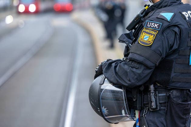 Montagsdemo Team Menschenrechte mit Gegendemonstration und Blockaden, Nürnberg, 27.07.2026 Ein Polizist der USK (Unterstützungskommando) in Einsatzmontur mit Bayern-Wappen hält einen Helm mit Visier in der Hand. Im Hintergrund sind weitere Einsatzkräfte sowie eine Straßenbahn zu erkennen. Nürnberg Bayern Deutschland *** Monday Demonstration by the Human Rights Team, featuring a counter-demonstration and roadblocks, Nuremberg, July 27, 2026 A police officer from the USK (Support Command) in riot gear bearing the Bavarian coat of arms is holding a helmet with a visor. In the background, additional law enforcement officers and a streetcar can be seen. Nuremberg, Bavaria, Germany 20260727-6V2A0167-M4000