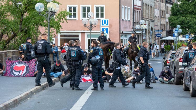 Montagsdemo Team Menschenrechte mit Gegendemonstration und Blockaden, Nürnberg, 27.07.2026 Polizeikräfte zu Pferd und zu Fuß sichern eine Sitzblockade in der Ludwigsstraße von Gegendemonstranten auf. Mehrere Personen sitzen auf der Straße, im Vordergrund ist ein Transparent der Antifa zu erkennen. Einsatzkräfte in Schutzausrüstung führen Blockierende von der Fahrbahn. Nürnberg Bayern Deutschland *** Monday Demonstration: Human Rights Team with Counter-Demonstration and Blockades, Nuremberg, July 27, 2026. Police officers on horseback and on foot are securing a sit-in blockade on Ludwigsstraße set up by counter-demonstrators. Several people are sitting on the street; and an Antifa banner can be seen in the foreground. Officers in 20260727-6V2A0472-M4000