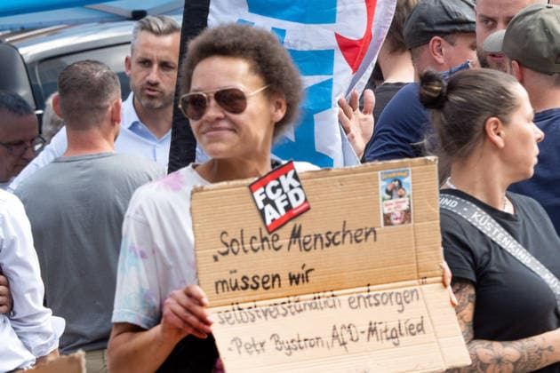 Gegendemonstrantin bei AfD-Wahlkampf mit Ulrich Siegmund, AfD Spitzenkandidat in Sachsen-Anhalt, AfD-Infostand in Magdeburg, 28. Juli 2026 Deutschland, Magdeburg, 28. Juli 2026, Gegendemonstrantin bei AfD Wahlkampf in der Magdeburger Innenstadt, mit Anti-AfD-Plakat, im Hinterund links Ulrich Siegmund, AfD-WSpitzenkandidat bei den Landtagswahlen in Sachsen-Anhalt am 6. September, Wahlkampfstand an der Ecke Goldschmiedebrücke - Breiter Weg, viele Wähler kommen, um ein Slfie mit dem Spitzenkandidaten zu machen, rechtsextreme Landespartei, Politiker, Politik, *** Counter-protester at an AfD campaign event with Ulrich Siegmund, the AfD’s top candidate in Saxony-Anhalt, AfD information booth in Magdeburg, July 28, 2026; Germany, Magdeburg, July