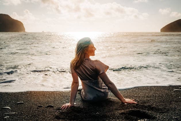 Woman sitting on a dark sand beach at sunset São Miguel, Açores, Portugal CR_FKNH260728-2086916-01 ,model released, Symbolfoto ,property released