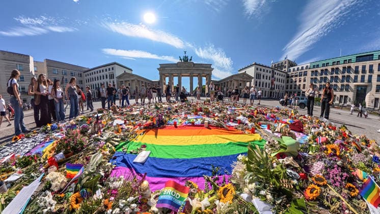 Zahlreiche Menschen haben vor dem Brandenburger Tor Blumen, Kerzen, Regenbogenfahnen niedergelegt und trauern um die Opfer des CSD-Anschlags, Mittwochnachmittag, Berlin, 29. Juli 2026 Deutschland, Berlin, 29. Juli 2026, die Sonne scheint über dem Gedenkort für die Opfer des CSD-Anschlags, zahlreiche Menschen haben vor dem Brandenburger Tor Blumen, Kerzen, Regenbogenfahnen niedergelegt, einen Erinnerungsort geschaffen, im Mittelpunkt liegt eine Regenbogenfahne mit einem Exemplar des Grundgesetzes, das Blumenmeer setzt ein sichtbares Zeichen gegen Hass und Gewalt, Szene am Mittwochnachmittag um 16:30 Uhr, knapp vier Tage nach dem islamistischen Terroranschlag im Tiergarten, bei dem ein Mensch starb und weitere teils schwer verletzt wurden,