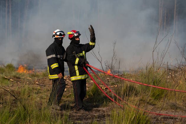 Wildfire Near Le Temple - Gironde Two firefighters coordinate hose deployment while battling an active wildfire near Le Temple, Gironde, southwestern France, on July 29, 2026. Smoke and flames spread through the low vegetation as crews work to contain the advancing fire.  Copyright: xSaptexFabrice ABACAx