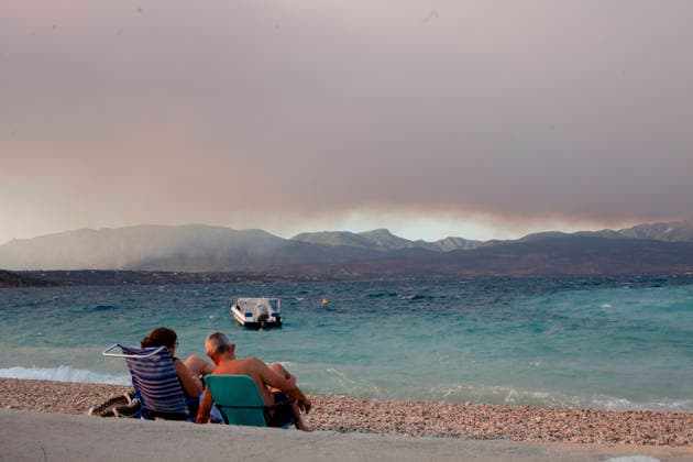 Wildfire Smoke and Strong Winds Hit Corinthia Coast People sit on a beach as smoke from a wildfire in Viotia rises above the mountains in Almiri, Corinthia, Greece on August 1, 2026. The smoke drifts across the Saronic Gulf from a wildfire burning in the neighboring regional unit of Viotia as firefighters continue efforts to contain the blaze. Almiri Corinthia Greece Copyright: xElvisxTakahashixMantellox