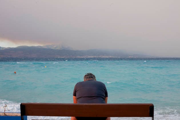 Wildfire Smoke and Strong Winds Hit Corinthia Coast A man sits on a beach as smoke from a wildfire in Viotia rises above the mountains in Almiri, Corinthia, Greece on August 1, 2026. The smoke drifts across the Saronic Gulf from a wildfire burning in the neighboring regional unit of Viotia as firefighters continue efforts to contain the blaze. Almiri Corinthia Greece Copyright: xElvisxTakahashixMantellox