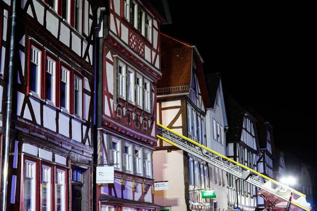 Feuer im Dachgeschoss eines Fachwerkhauses Flammen schlagen aus dem Fenster Feuerwehr riegelt enge Altstadt ab Am 03.08.2026 brannte gegen 21:00 Uhr ein Fachwerkhaus in der Oberstadt 18 in der Altstadt von Lich. Der Brand betraf das Obergeschoss und den Dachbereich des Gebäudes, es kam zu starker Rauchentwicklung und Flammenaustritt. Beim Eintreffen der Feuerwehr befand sich niemand mehr im Gebäude. Die Freiwillige Feuerwehr Lich leitete Außen- und Innenangriff ein und baute wegen der engen Altstadtbebauung eine Riegelstellung mit der Drehleiter zum Schutz der Nachbarhäuser auf. Lich Hessen Deutschland *** Fire in the attic of a half-timbered house; flames are shooting out of the window; firefighters cordon off the narrow old t