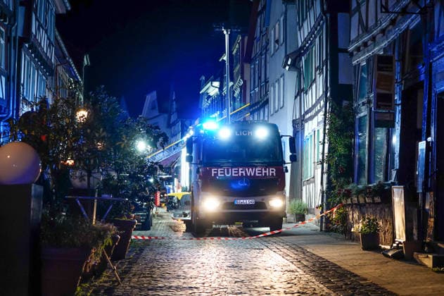 Feuer im Dachgeschoss eines Fachwerkhauses Flammen schlagen aus dem Fenster Feuerwehr riegelt enge Altstadt ab Am 03.08.2026 brannte gegen 21:00 Uhr ein Fachwerkhaus in der Oberstadt 18 in der Altstadt von Lich. Der Brand betraf das Obergeschoss und den Dachbereich des Gebäudes, es kam zu starker Rauchentwicklung und Flammenaustritt. Beim Eintreffen der Feuerwehr befand sich niemand mehr im Gebäude. Die Freiwillige Feuerwehr Lich leitete Außen- und Innenangriff ein und baute wegen der engen Altstadtbebauung eine Riegelstellung mit der Drehleiter zum Schutz der Nachbarhäuser auf. Lich Hessen Deutschland *** Fire in the attic of a half-timbered house; flames are shooting out of the window; firefighters cordon off the narrow old t