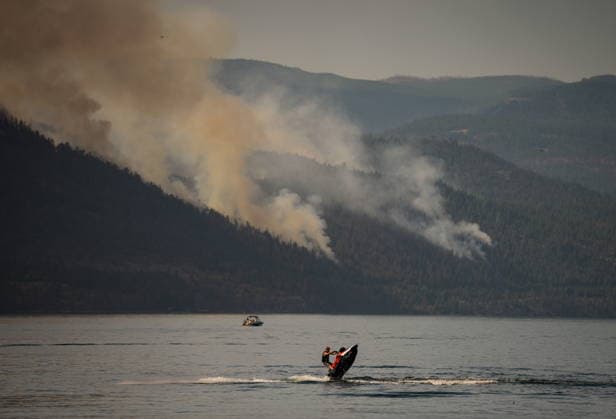 August 3, 2026, Lake Country, Bc, CANADA: A person rides a personal watercraft on Okanagan Lake, in Lake Country, B.C., as the Quilpituk Creek wildfire burns on the mountainside across the lake in near Fintry, on Monday, Aug. 3, 2026. Lake Country CANADA  - ZUMAc35_ 20260803_zaf_c35_057 Copyright: xDarrylxDyckx