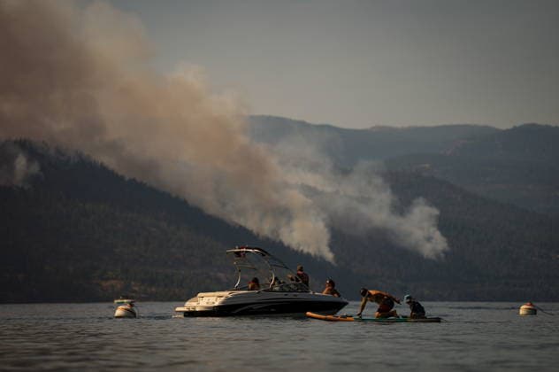 August 3, 2026, Lake Country, Bc, CANADA: A man prepares to use a paddleboard with a child as people sit on a boat on Okanagan Lake, in Lake Country, B.C., while the Quilpituk Creek wildfire burns on the mountainside across the lake, near Fintry, on Monday, Aug. 3, 2026. Lake Country CANADA  - ZUMAc35_ 20260803_zaf_c35_062 Copyright: xDarrylxDyckx
