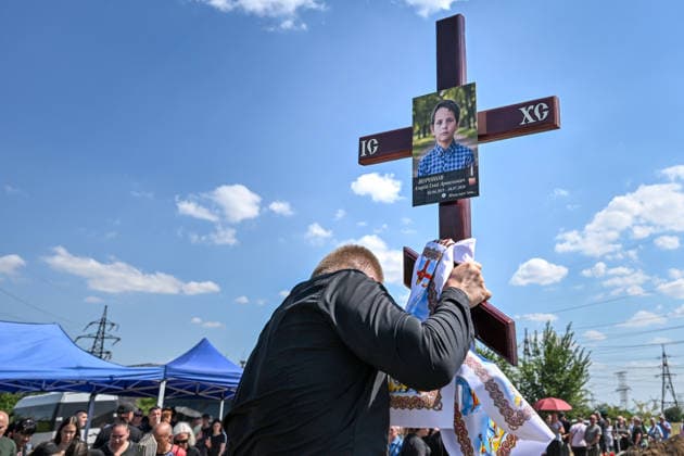 A man holds the cross with the photo of Azarii Ilai, 11, during the funeral of members of the Voronov family, killed when a Russian Iskander-M ballistic missile directly struck their home on the night of Thursday, July 30, Radushne settlement, Kryvyi Rih district, Dnipropetrovsk region, Ukraine, August 3, 2026. Five family members whose identities have been officially confirmed were laid to rest: parents Artem, 47, and Olena, 41, together with their children Mark, 17, Azarii Ilai, 11, and Emiliia, 6. Five other children who were in the house that night - Zakhar, Dominika, Viorika, Federika and one-and-a-half-year-old grandson Artem - are still officially listed as missing. Rescuers recovered 17 body fragments from the rubble, and complex fo  Copyright: xDmytroxSmolienkox