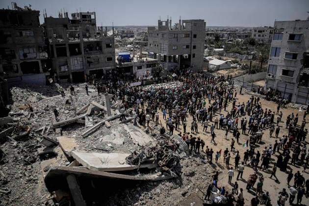 Gaza City Mass Funeral August 3 2026 Mourners gather around rows of bodies wrapped in Palestinian flags amid destroyed buildings during a mass funeral procession in the Al-Sabra neighborhood of Gaza City, Gaza Strip, on August 4, 2026. The remains of 112 members of the Abu Sharia and Al-Hasayneh families were recovered from the rubble of their home following an Israeli strike. Relatives stated the attack claimed the lives of more than 300 people. The bodies were buried at Al-Maamadani Cemetery as military operations continue across the territory. Gaza Gaza Strip Palestinian Territories Copyright: xMohammedxMxSkaikx