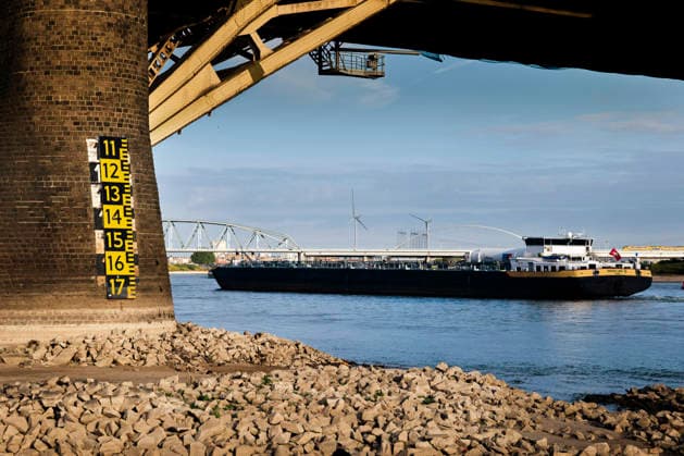 August 6, 2026, Nijmegen, Gelderland, Netherlands: Under the WAALBRUG near NIJMEGEN, a cargo vessel passes the exposed rocky riverbank and a water level gauge on the bridge pillar, where the current low mark clearly shows how far the WAAL has dropped. In the background the railway bridge spans this main Dutch branch of the RHINE, which is experiencing historic low water levels due to prolonged drought, forcing inland shipping to sail with sharply reduced loads. Credit : ZUMA Press Nijmegen Netherlands - ZUMAv145 20260806_zip_v145_005 Copyright: xNorbertxVoskensx