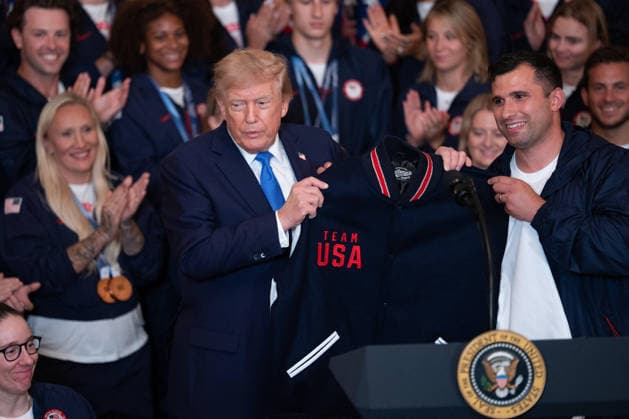 President Trump Hosts Team USA Olympians at White House United States President Donald J Trump is gifted a Team USA jacket and shoes in the East Room of the White House in Washington, DC, USA, on Thursday, August 6, 2026. President Trump is hosting a ceremony for Team USA Olympians who competed in the 2026 Olympic Winter Games in Italy. Credit: Aaron Schwartz Pool via CNP Washington District of Columbia United States  Copyright: xPool ABACAx