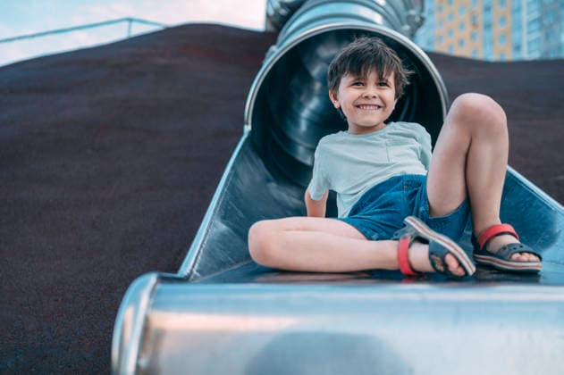 A smiling boy rides a metal slide at the outdoor playground model released, Symbolfoto, ANAF06554