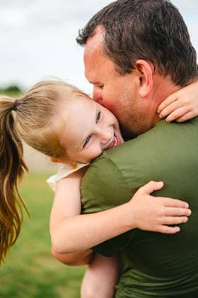 A father affectionately hugs his smiling daughter outdoors model released, Symbolfoto, IGEF01097