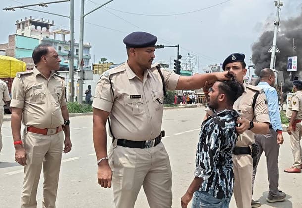 PATNA, INDIA - AUGUST 7: Police officials detains a protestor after vehicles were set ablaze following the death of a man in a road accident on August 7, 2026 in Patna, India. A speeding bus struck and fatally ran over a 22-year-old local resident Manish Kumar along National Highway 30. Incensed by the fatal hit-and-run incident, angry residents and eyewitnesses staged a road blockade, vandalized passing vehicles including public transport bus, three police vehicles, and several two-wheelers. The mob also pelted stones at responding law enforcement teams.(Photo by Santosh Kumar Hindustan Times) Angry Mob Torches Bus, Police Vehicles After Youth Killed by Speeding Bus In Patna