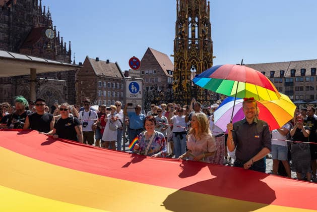 CSD Nürnberg 2026 Nürnberg Pride Week, Nürnberg, 08.08.2026 Teilnehmer tragen eine große Regenbogenflagge beim Christopher Street Day durch die Nürnberger Innenstadt, im Hintergrund der Schöne Brunnen. Oberbürgermeister Marcus König (CSU) mit Ehefrau Anke sowie die Landtagsabgeordnete Verena Osgyan (Bündnis 90 Die Grünen) laufen an der Flagge mit, mehrere Teilnehmer halten bunte Regenschirme. Nürnberg Bayern Deutschland *** CSD Nuremberg 2026 Nuremberg Pride Week, Nuremberg, August 8, 2026 Participants carry a large rainbow flag through downtown Nuremberg during Christopher Street Day, with the Schöne Brunnen fountain in the background; Mayor Marcus König (CSU) and his wife Anke, as well as State Parliament Representative V 20260808-286A4694-M4000
