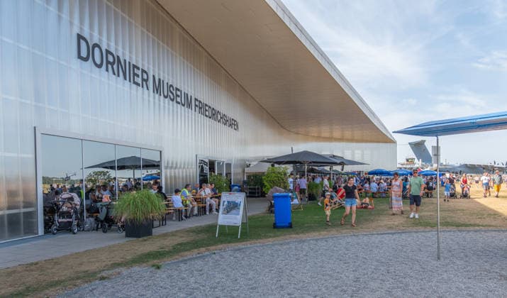 Friedrichshafen DO DAYS Flugwochenende im Dornier Museum Friedrichshafen 09.08.2026 Auch der Aussenbereich mit Gastronomie am Dornier Museum Friedrichshafen ist waehrend der DO DAYS gut gefuellt. Besucherinnen und Besucher sitzen an Tischen, gehen ueber das Veranstaltungsgelaende und halten sich vor der Fassade des Museums auf. DO DAYS Flugwochenende und Sommerfest im Dornier Museum Friedrichshafen, Friedrichshafen, Baden Wuerttemberg, Deutschland, 09.08.2026. Luftfahrt Veranstaltung. Editorial use only. *** Friedrichshafen DO DAYS Aviation Weekend at the Dornier Museum in Friedrichshafen, August 9, 2026. The outdoor area with food and beverage options at the Dornier Museum in Friedrichshafen is also bustling during the DO DAYS; visitors Copyright: xEibner-Pressefotox EP_EER