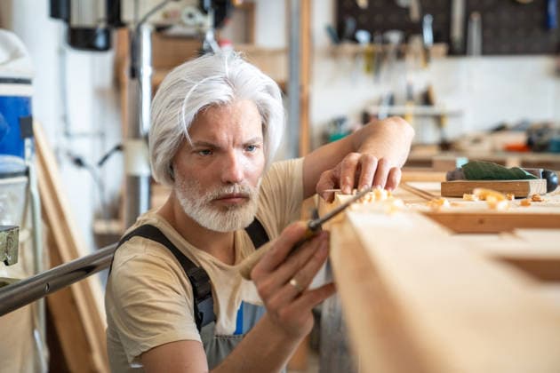 Erfahrener Handwerker, der an seiner Werkbank an einer alten Holztür arbeitet und deren Oberfläche sorgfältig prüft Experienced man crafter working with vintage wooden door at workbench mindfully checking surface, thoughtful craftsman woodworker in carpentry workshop examining wood during reconstruction process. (License=RF) ,model released, Symbolfoto Copyright: xZoonar.com DmitriixMarchenkox 25383764 ,model released, Symbolfoto ,property released