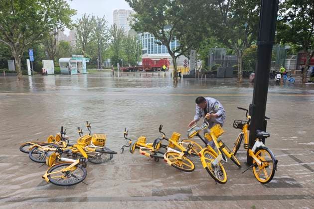 SHANGHAI, CHINA - AUGUST 09: Maintenance workers lift shared bicycles knocked over by wind and rain amidst flooding caused by Typhoon Dolphin on August 9, 2026 in Shanghai, China. The city was impacted by heavy rainfall and strong winds as Typhoon Dolphin made landfall.  Copyright: xVCGx 111659005875