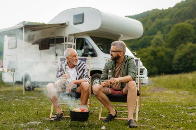 Father and adult son grilling beside camper during family RV vacation. Father and adult son grilling beside camper during family RV vacation. Camping in nature. model released