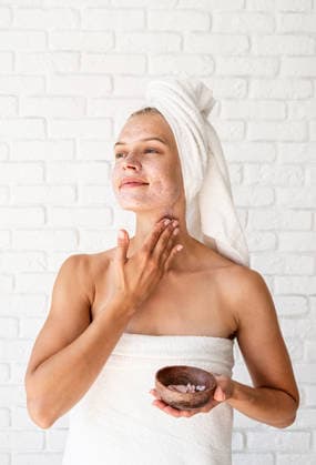 Eine fröhlich lächelnde junge Frau in weißen Badetüchern, die sich ein Peeling auf Gesicht und Hals aufträgt attractive smiling woman applying scrub on her skin. Facial cleansing concept. Spa and beauty. Natural cosmetics (License=RF) ,model released, Symbolfoto Copyright: xZoonar.com IlonaxShorokhovax 25393602 ,model released, Symbolfoto ,property released