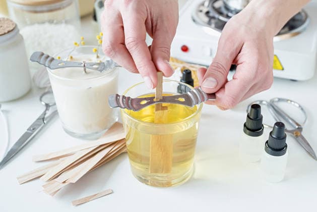 Nahaufnahme einer Frau, die den Holzdocht in eine handgemachte Kerze steckt Creative hobby of candle making at home. Woman making decorative aroma candle at table, setting wooden wick into glass with melted soy wax (License=RF) Copyright: xZoonar.com ILONAxSHOROKHOVAx 25393609